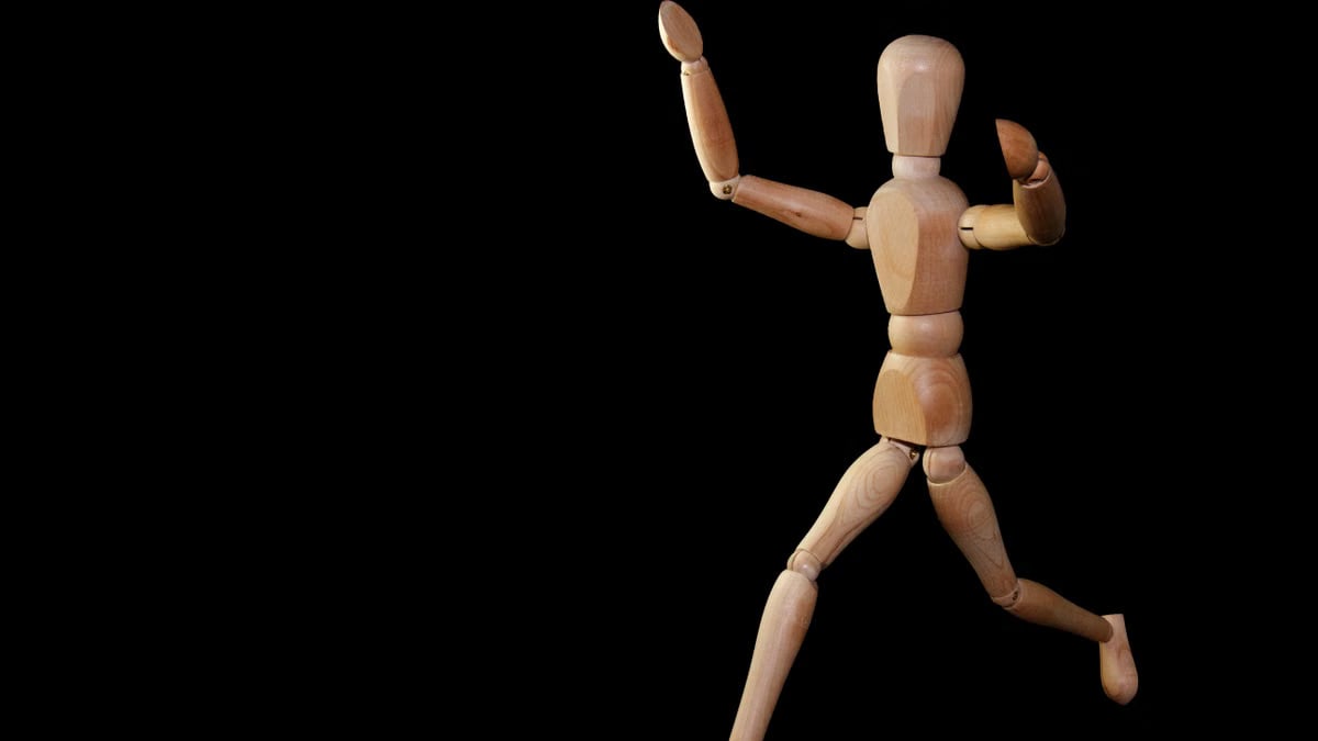 Wooden mannequin artfully posed against a black backdrop, showcasing movement.
